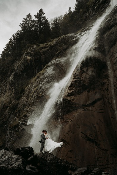 bride and groom standing under waterfall