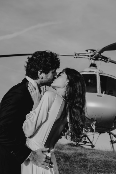 black and white photo of bride and groom kissing in front of helicopter