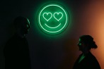 groom looking at bride in front of big neon smiley face