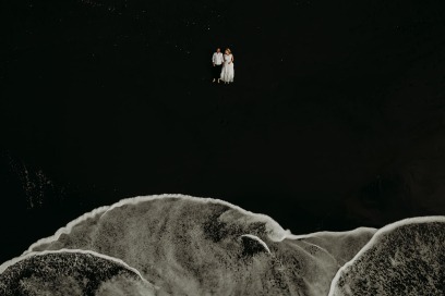 bride and groom lying on a black beach while white waves roll in
