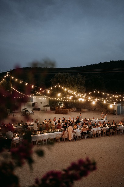 group of friends sitting at long tables with stringlights, having dinner during blue hour 