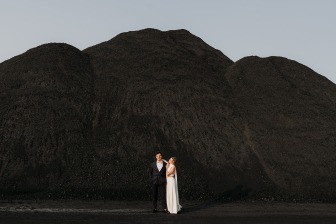 married couple posing in front of black sand mountains