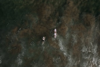 couple paddling out on their surf boards in wedding attire