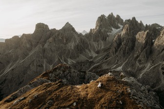bride and groom walking together on a grassy mountain ridge, dwarfed by the dramatic peaks of the Dolomites surrounding them