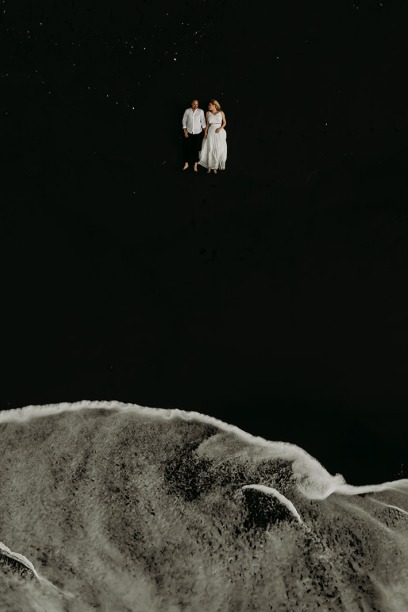 bride and groom lying on a black beach while white waves roll in
